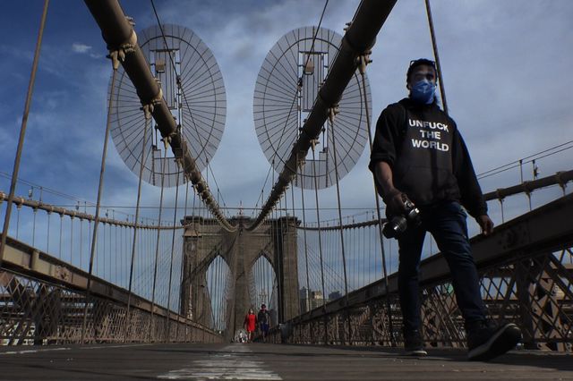 A photo of a person walking across the Brooklyn Bridge in a mask